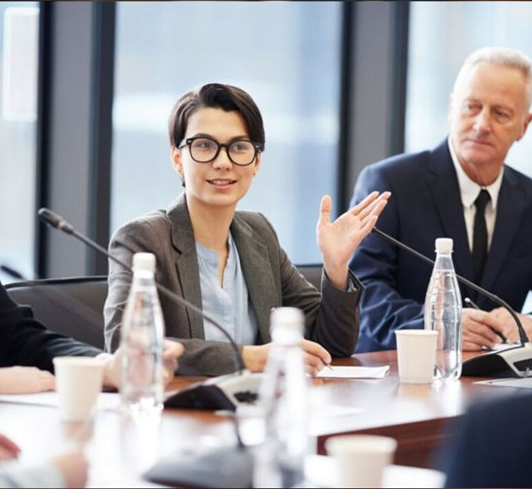 A professional woman in a business suit leads a discussion during a meeting, while colleagues listen attentively.