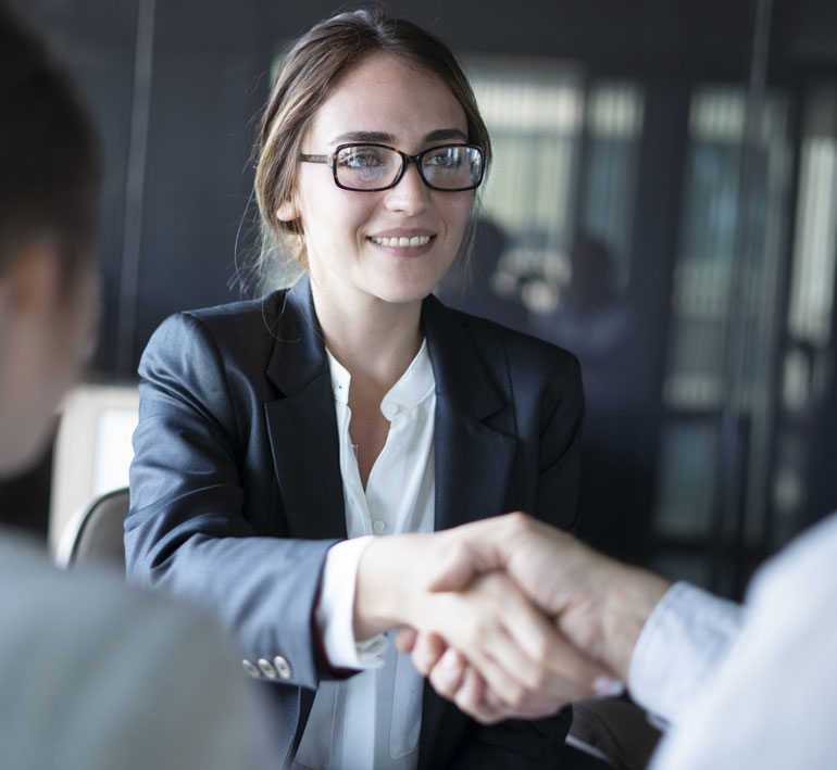 A smiling businesswoman wearing glasses shakes hands during a meeting, reflecting positive business negotiations.