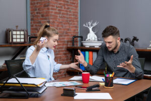 Two colleagues in a heated argument during a workplace meeting, visibly frustrated with one another.